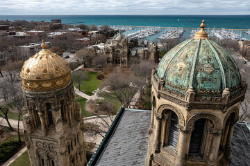 Two ornate historical towers with detailed domes overlooking a marina and cityscape near a large body of water.