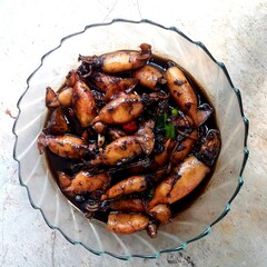 delicious Indonesian-style squid dish cooked with soy sauce, garlic, and spices, served in a glass bowl on a rustic table. Traditional seafood cuisine, rich flavor, and authentic Asian home cooking.