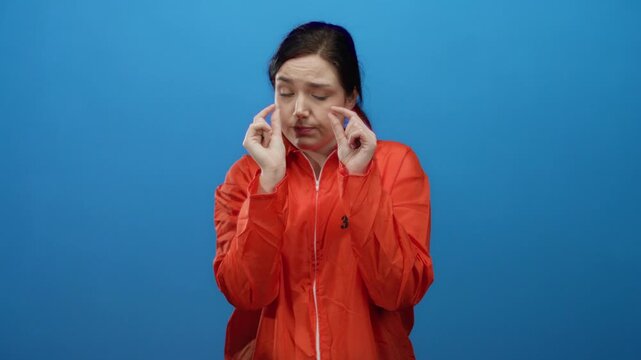 Woman in orange prison jumpsuit making small hand gesture against blue background signifies something minimal or insignificant.
