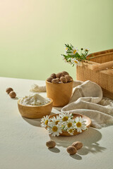 Natural styled setup of shea butter and chamomile bouquet with nuts on soft green surface. Perfect for spa, beauty, and skincare branding visuals.