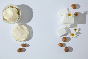 Overhead view of shea butter cream in bowls with chamomile and shea nuts. Clean setup for organic cosmetic ingredients and skincare photography. Copy space