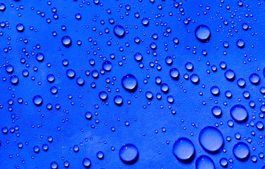 Closeup macro of transparent water droplets on a bright blue surface. Shows natural condensation patterns and liquid freshness. Ideal for hydration, aqua concepts, and abstract designs.