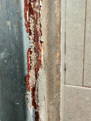 Close-up view of a rusty metal frame with peeling paint and cement residue, showing signs of corrosion and deterioration