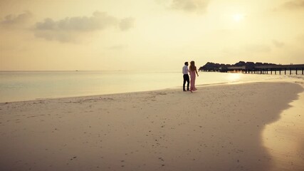 Elegant couple dancing and walking hand-in-hand along a tropical beach during sunset, enjoying a fun intimate moment together. Captures barefoot romance and the magic of a luxurious seaside escape. - Powered by Adobe