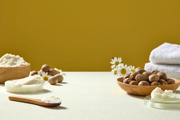 Flat composition of shea butter, nuts, chamomile flowers and towels on table, spa-inspired shot against yellow background for wellness brands.