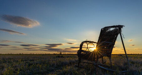 Vintage creepy rocking chair at sunset next to a dirt path to nowhere in the outback of the...