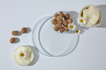 Overhead shot of shea butter cream, shea nuts, and flowers arranged with glass props, leaving space for cosmetic product or design placement. Space for display product