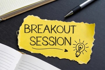 Torn yellow paper spelling 'BREAKOUT SESSION' nearest with Light Bulb Icon arranged neatly on a dark desk, beside a book and a sleek pen for writing