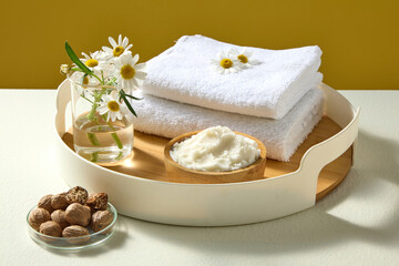 Wooden tray styled with shea butter, nuts, towels and chamomile flowers, clean minimalist spa composition for skincare branding displays.