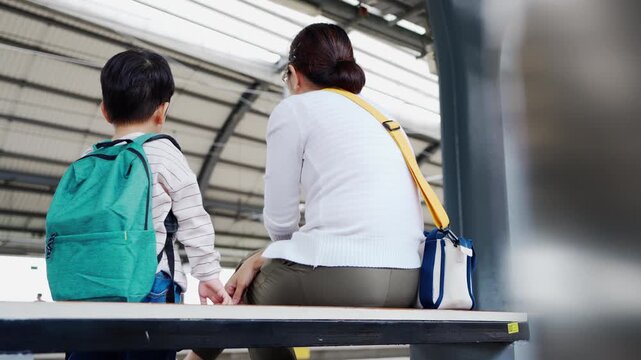 Asian mother and child boy sitting close at skytrain station, sharing quiet travel moment and enjoying time together before trip