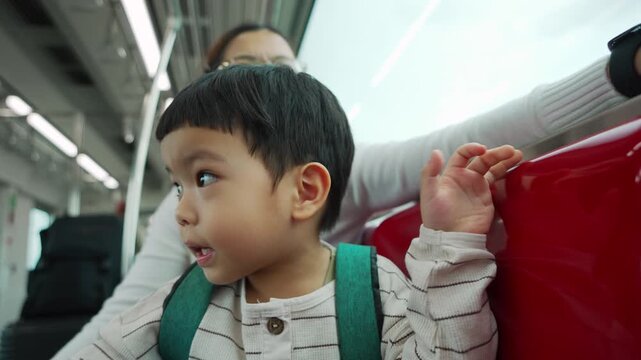 Asian child looking around skytrain with excitement, mother smiling nearby enjoying family travel and happy city ride together
