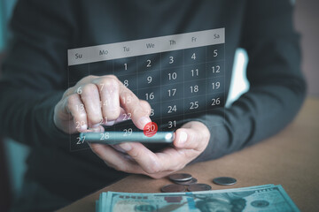 A person is using a smartphone with a virtual calendar and a red circle marking the 30th day. Financial planning, managing budget, expenses, and deadlines, paying bill, or upcoming payment dates.