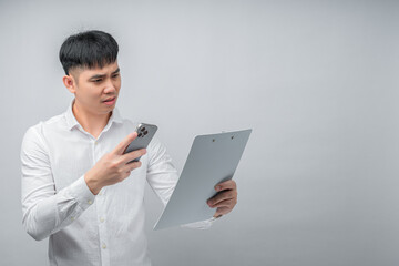 A handsome Asian young man expresses shock and sadness while reviewing a financial document and using a smartphone for checking. Concept for business, finance, technology and lifestyle themes.