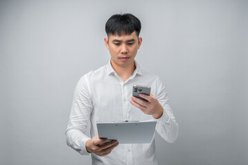 A handsome Asian young man expresses shock and sadness while reviewing a financial document and using a smartphone for checking. Concept for business, finance, technology and lifestyle themes.