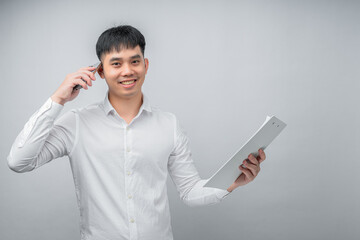 A handsome Asian young man smiling happily while reviewing a financial document and using a smartphone for checking information. Concept for business, finance, technology and lifestyle themes.