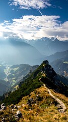 Naklejka premium Mountain path winding to a peak, valley and distant mountains visible below a partly cloudy sky