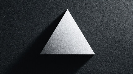 A white textured triangle sits on a dark background casting a stark shadow in a minimalist high-contrast composition highlighting light and geometric form