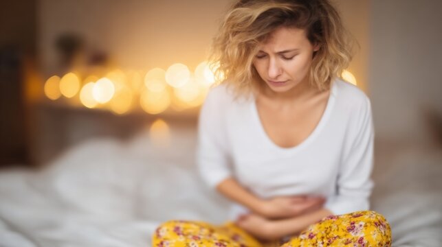 Woman sitting on bed experiencing discomfort in cozy, warm setting