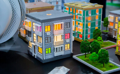Fototapeta premium Prototype of building printed on 3D printer from melted plastic. A 3D-printed building prototype. House created on 3D printer with gray walls, gray roof and illuminated windows and balconies.
