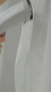 Vertical Screen: A person demonstrates steaming a white shirt to remove wrinkles. The process is quick and effective, showcasing a handy cleaning technique without an iron.