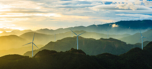 Wind turbines generating clean and sustainable electricity on the green mountains during a beautiful misty sunrise