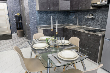 A modern kitchen and dining area feature a glass table set for four, complemented by a grey kitchen with a patterned backsplash and sleek appliances