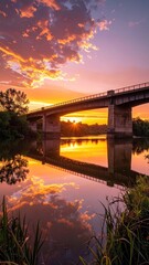 Fototapeta premium Dramatic Sunset Over River Reflecting Bridge and Glowing Sky in Warm Orange and Purple Hues Nature Photography