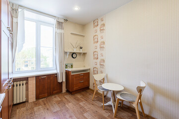 Cozy kitchen featuring wooden cabinets, a white table with chairs, and natural light from a window. The room has a warm, inviting atmosphere