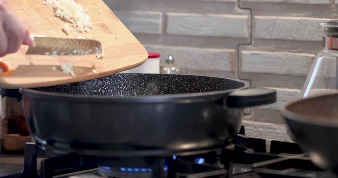 Cook throws radishes cut into small pieces into boiling pan on gas stove.