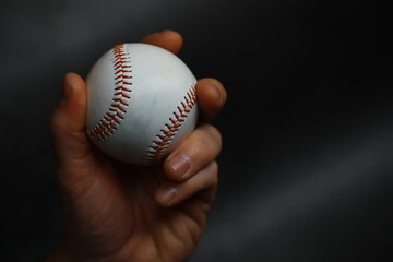 Close-Up of Hand Holding Baseball Against Dark Background