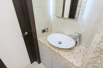 Modern bathroom interior with a white oval sink, chrome faucet, mosaic countertop, and elegant mirror. Neutral tones create a clean, sophisticated look