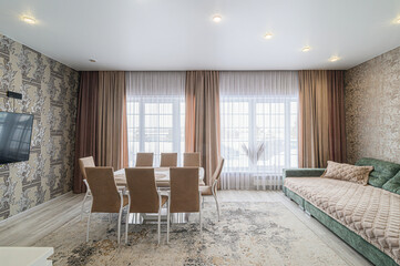 A well-lit living room with a dining area featuring a table, chairs, sofa, and large windows with elegant curtains.