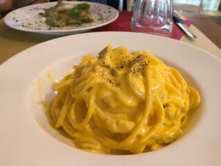 A bowl of pasta with yellow sauce and cheese. There is a knife and a fork on the table