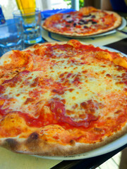 Pizza with salami on plates A slice of pepperoni pizza. The pizza is on a white plate. There are four other slices of pizza on the table