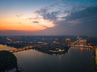 Naklejka premium Suizhou city lights glow during twilight over the Hubei Province river as bridges span the water.