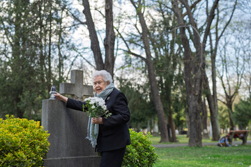 Old lady remembering a loved one at a grave.