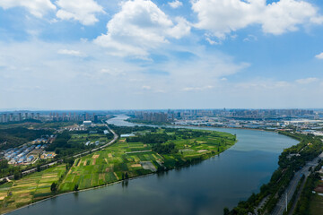 Suizhou City Hubei Province China river landscape showing city buildings and green fields under a bright sky with clouds.