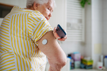Senior woman checking glucose levels with smartphone.