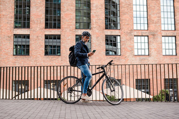 Fototapeta premium City commuter riding bike from work, reading text message on phone.