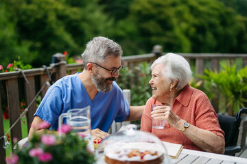 Caregiver spending time with elderly woman, drinking coffee and talking.