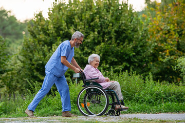 Fototapeta premium Male home nurse taking care of elderly woman in wheelchair.