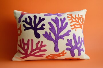 A decorative throw pillow showcases a vibrant design of embroidered coral, highlighted in shades of purple, orange, and pink, set against a natural cream background.