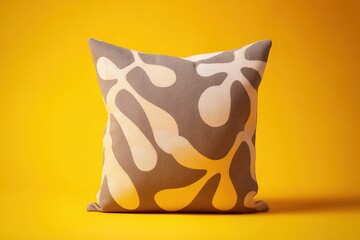 A decorative throw pillow, featuring a unique abstract pattern in muted earth tones, sits against a bright yellow backdrop.