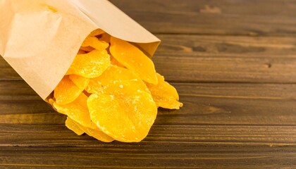 Dried mango slices in brown paper bag on wooden table
