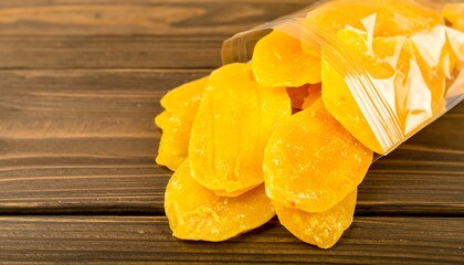 Dried mango slices in clear plastic bag on wooden surface