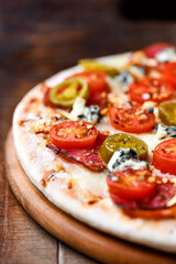 Pizza with salami, jalapeno pepper, cherry tomatoes and mozzarella cheese. Soft focus.	