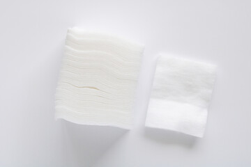Top view of a stack of white cotton pads and a single piece laid beside it on a clean white background.