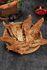 Dried bamboo shoots in woven basket with fresh vegetables and chilies on dark stone background