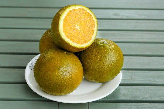 Fresh Orange Citrus Fruit Sliced on White Plate Green Wood Background - Powered by Adobe