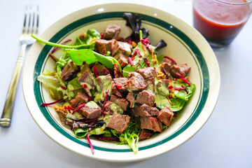 Refreshing cold steak salad, loaded with greens, shredded beets, and creamy dressing—served alongside a bold glass of fresh tomato juice for a nutrient-rich bite.